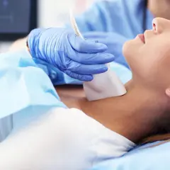 Lekarz wykonuje badanie USG tarczycy, które jest formą diagnostyki obrazowej. Pacjentka leży spokojnie podczas procedury.