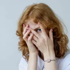 Rudowłosa dziewczyna z niebieskimi oczami zakrywa twarz dłońmi, jakby walczyła z fobią.