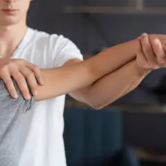 Fizjoterapeuta pomaga pacjentce z bólem łokcia golfisty, wykonując delikatne ćwiczenia rozciągające przedramię.