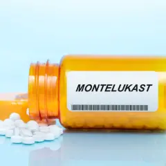 Pomarańczowa buteleczka z lekami na astmę, z etykietą "MONTELUKAST" i rozsypanymi tabletkami.