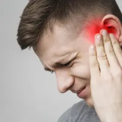 Mężczyzna z bólem ucha, czerwony obszar wskazuje na problem. Czas umówić wizytę u lekarza od uszu.