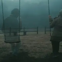 Mglisty poranek na placu zabaw. Kobieta na huśtawce, obok niej widmo mężczyzny, jakby syndrom trzeciego człowieka.