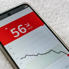 Niski poziom glukozy 56 mg/dL na ekranie telefonu, wskazujący na hipoglikemię reaktywną. Wykres pokazuje gwałtowny spadek.