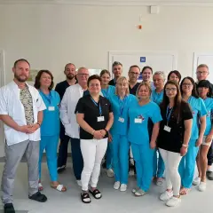 Grupa lekarzy i pielęgniarek w uniformach medycznych pozuje do zdjęcia w szpitalnym korytarzu.