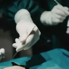 Dłonie chirurga i anestezjologa w białych rękawiczkach przygotowują narzędzia do operacji.