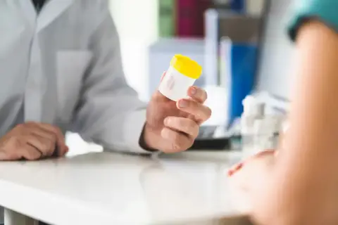 Lekarz w białym fartuchu podaje pacjentowi pojemnik na badanie kału.