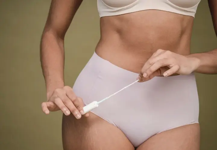 Kobieta trzymająca tampon. Zastanawiasz się, ile może się spóźniać okres? To normalne, że cykl menstruacyjny bywa nieregularny.