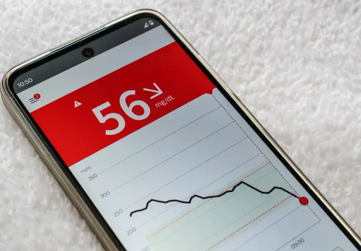 Niski poziom glukozy 56 mg/dL na ekranie telefonu, wskazujący na hipoglikemię reaktywną. Wykres pokazuje gwałtowny spadek.